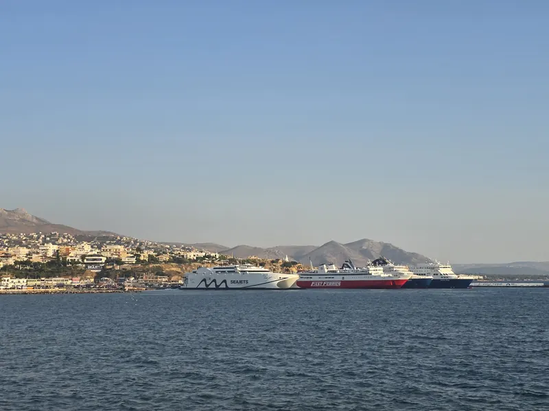 Ferries lined up in Rafina port in warm light, a white Seajets fast ferry and a red Fast Ferries ship among them, with the town on the hillside behind
